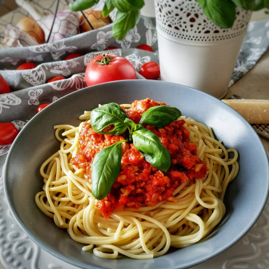 makaron spaghetti z sosem bolognese udekorowany listkami bazylii